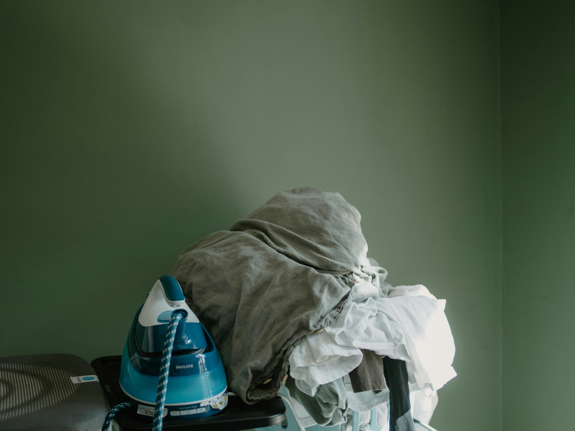 Ferro de passar e pilha de roupa pronta para acabamento.