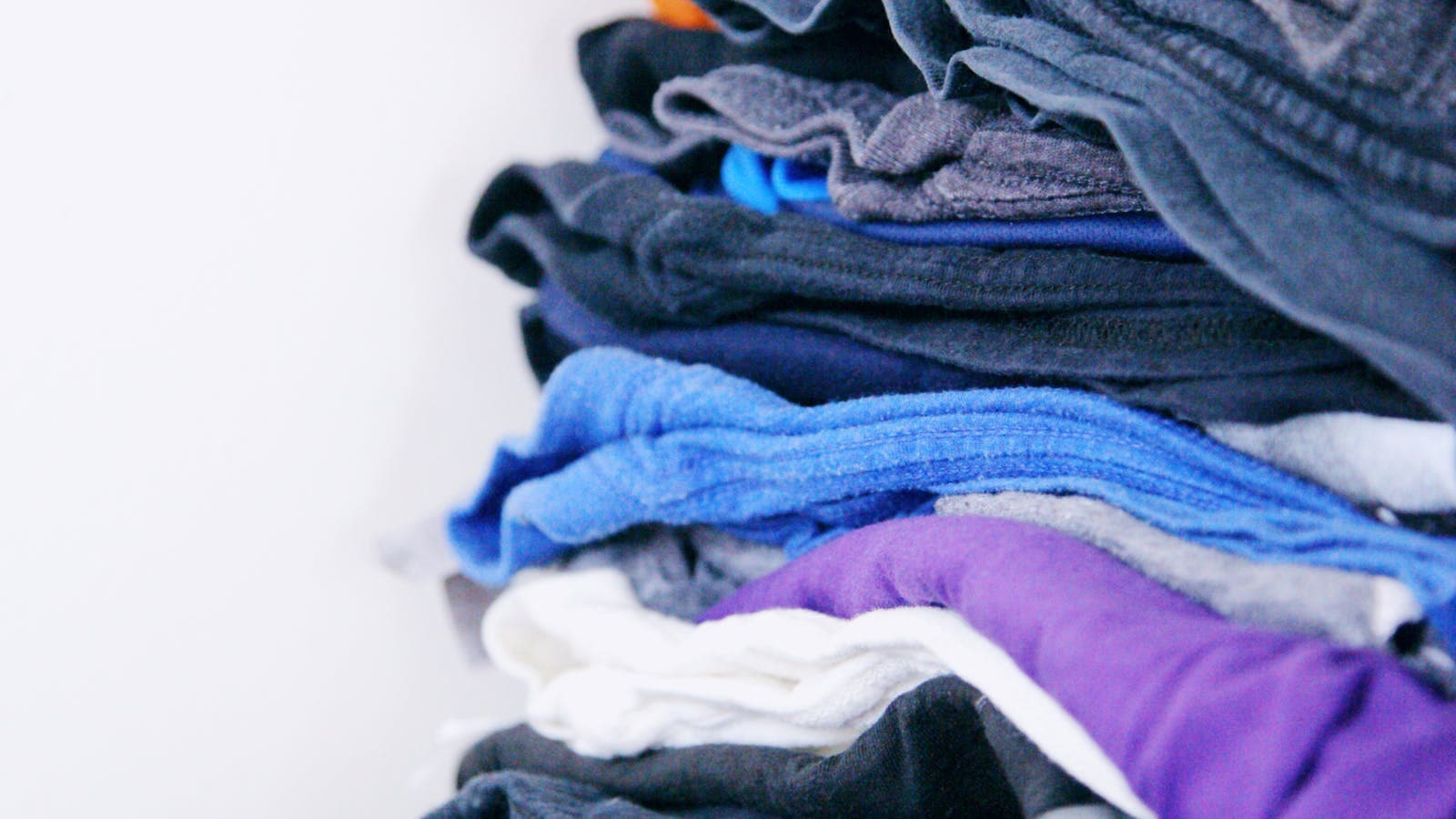 Roupas dobradas em tons coloridos para organizacao do guarda-roupa.